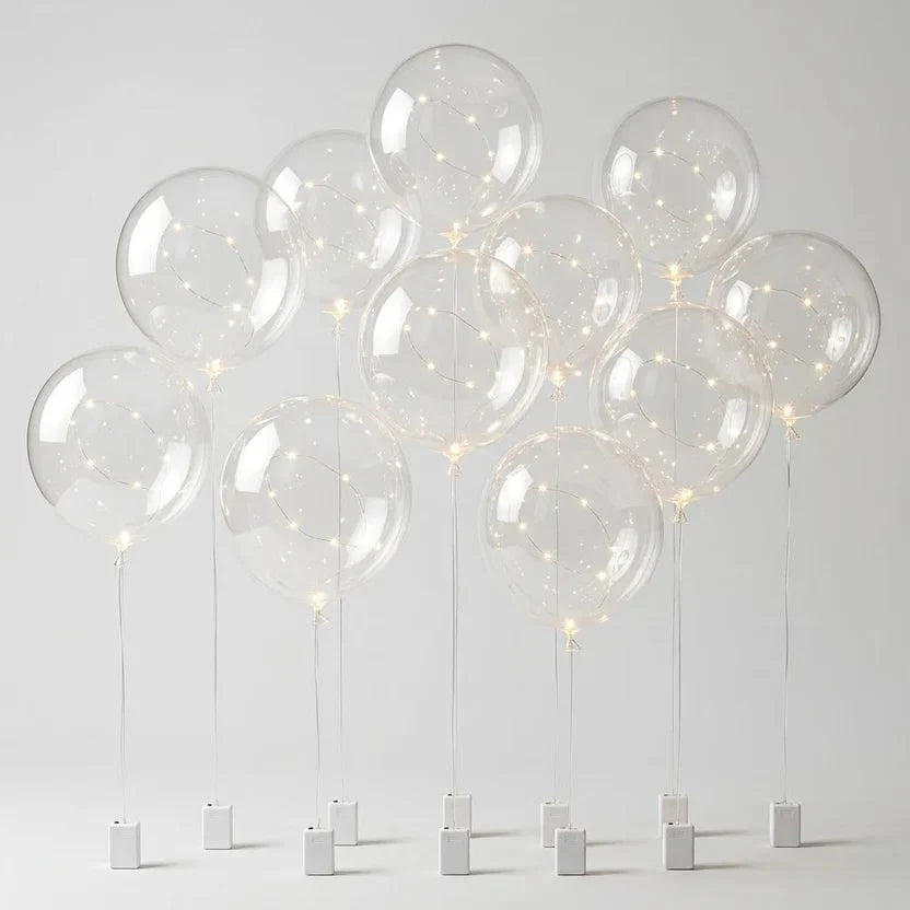 Zehn transparente Ballons mit Lichterkette an dünnen Schnüren, jeweils mit kleinem weißem Batteriefach, vor hellem 8