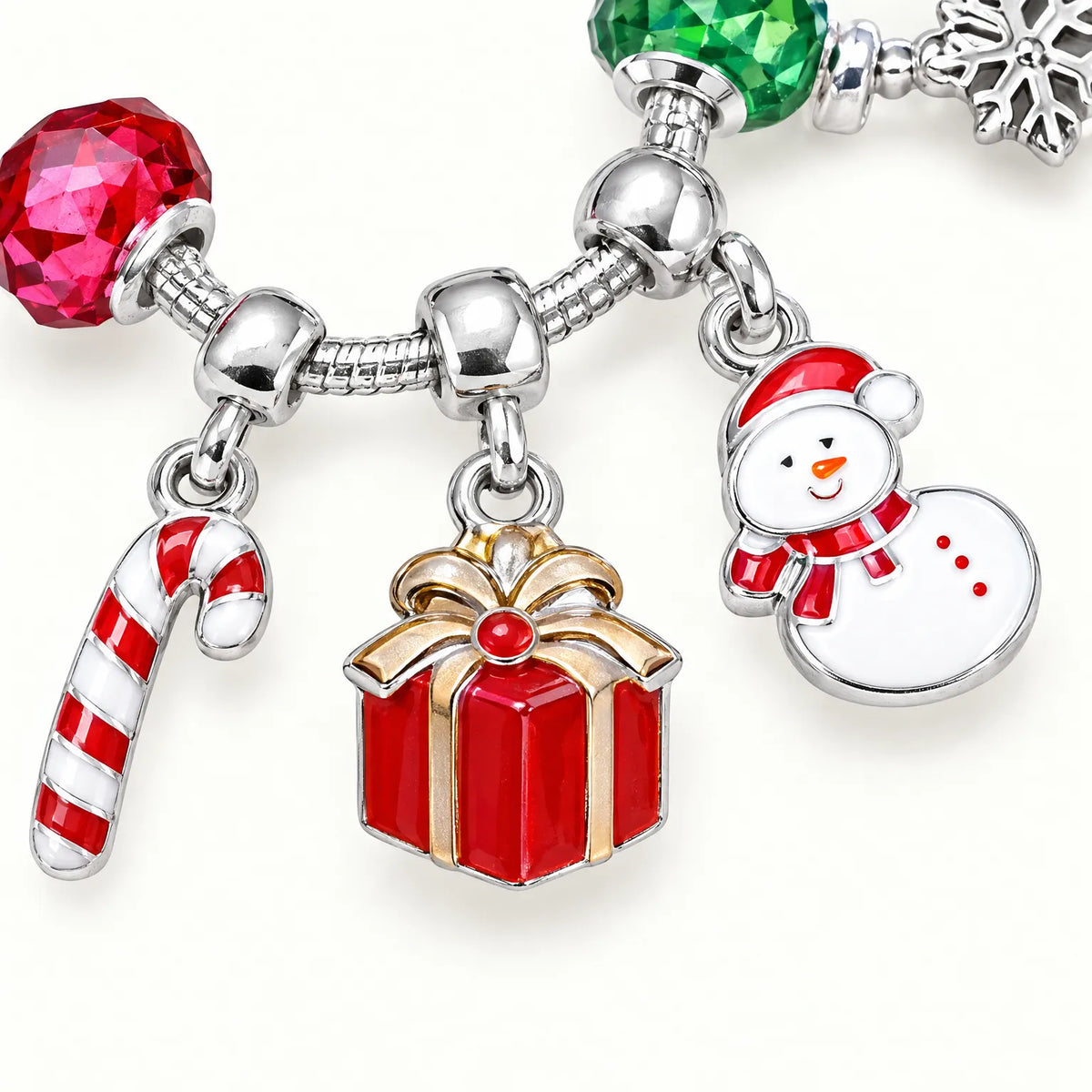 Nahaufnahme eines Armbands mit emailliertem Zuckerstangen-, Geschenk- und Schneemann-Anhänger zwischen einer facettierten roten und einer grünen Glasperle. 3