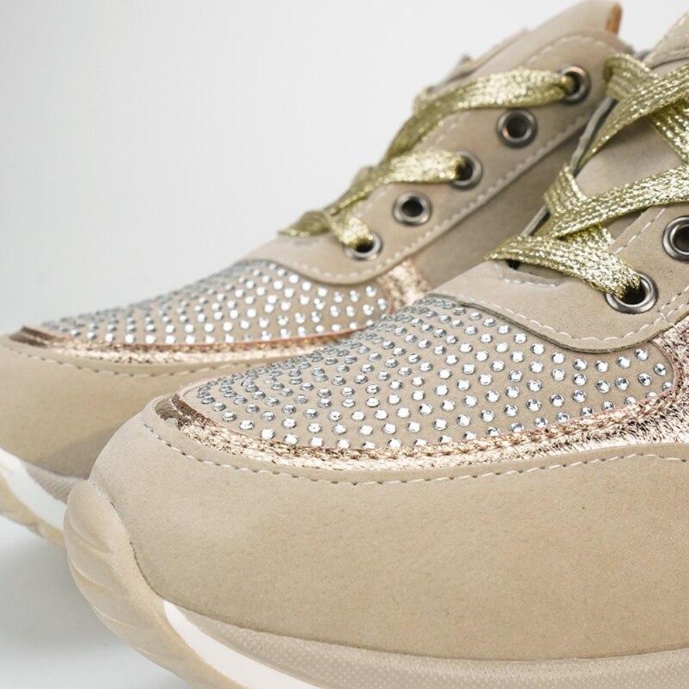 Nahaufnahme der Schuhspitzen mit Strasssteinen, goldfarbenen Schnürsenkeln und abgerundeter Kappe an den beigen Schuhen.