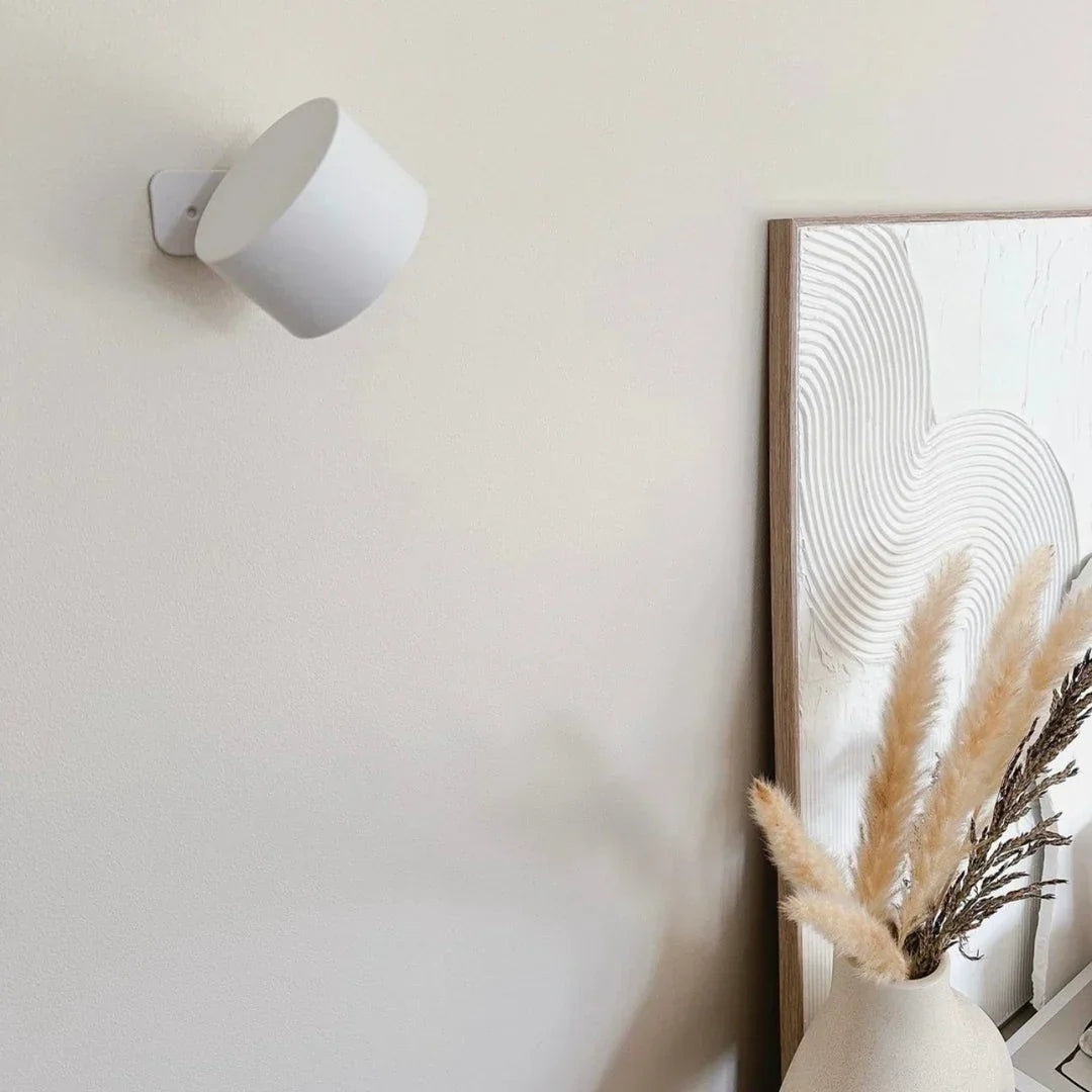 Ausgeschaltete weiße Wandleuchte an heller Wand neben einem Bild und einer Vase mit Pampasgras 16
