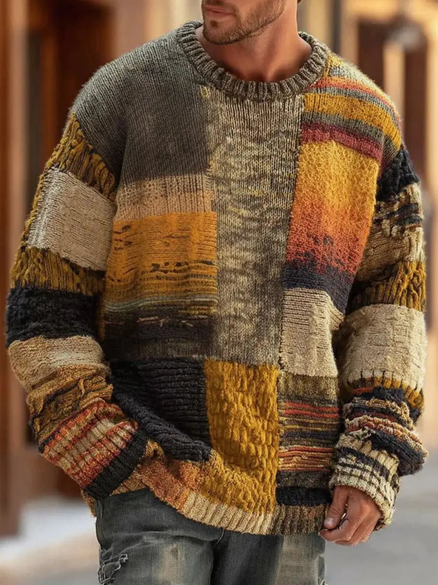 Mann trägt den Rundhalspullover in Erdtönen mit grob gestrickten Patchwork-Feldern, Frontansicht auf einer Straße 1