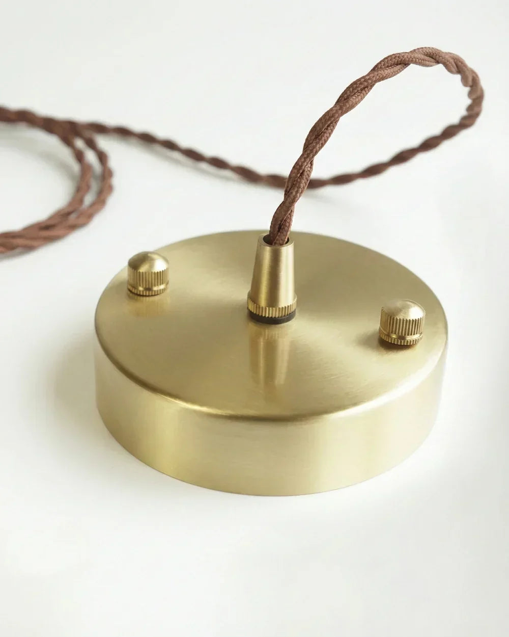 Runde Deckenrosette aus gebürstetem Messing mit braunem, gedrehtem Stoffkabel.