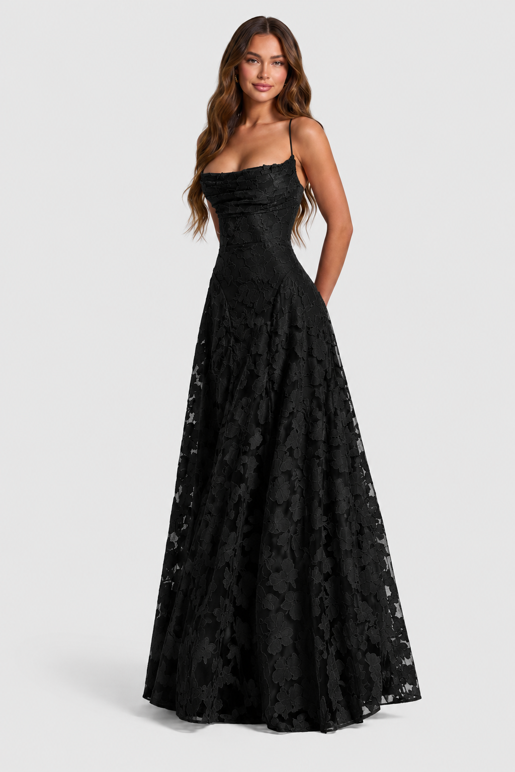 Model in schwarzem bodenlangem A-Linien-Kleid mit Blumenspitze, dünnen Trägern und drapiertem Ausschnitt, Dreiviertelansicht von vorne, die Hände hinter dem Rüc 21