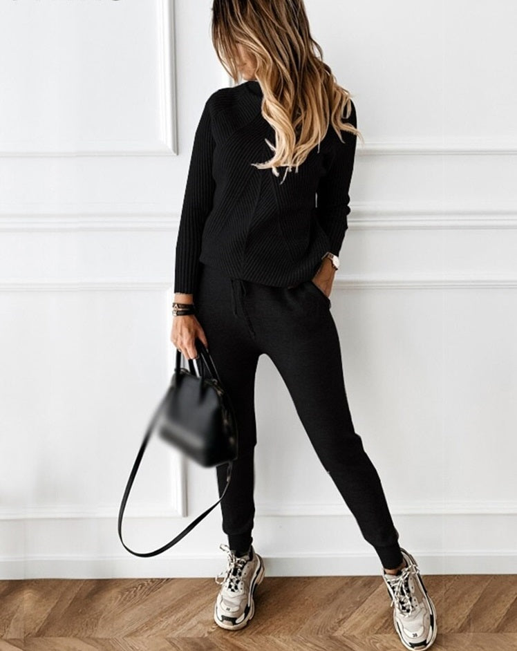 Frau in schwarzem Strickpullover und Jogginghose, trägt Sneakers und schwarze Handtasche.