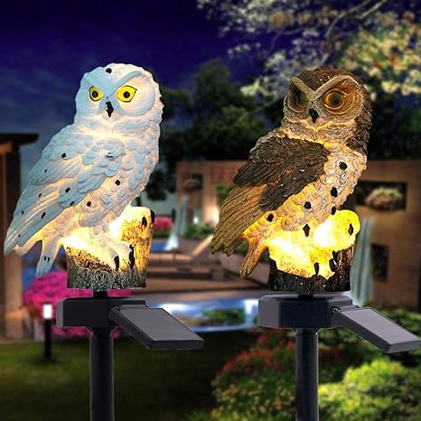 Weiße und braune Eule nebeneinander mit warmem Licht am Sockel und Solarpanel im Garten.
