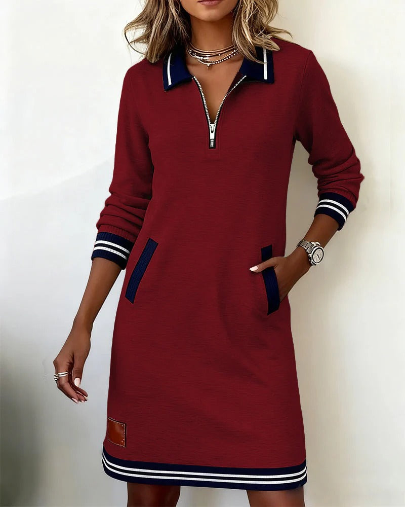 Weinrotes Kleid mit dunkelblauem Kragen und Taschenbesätzen, Reißverschluss vorne, vom Model mit einer Hand in der Tasche getragen. 5