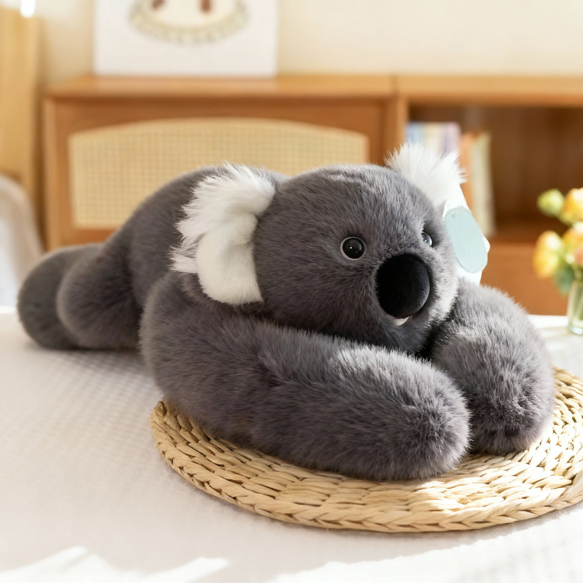 Graues Koala-Plüschtier mit weißen Ohren und großer schwarzer Nase auf einer Bastmatte