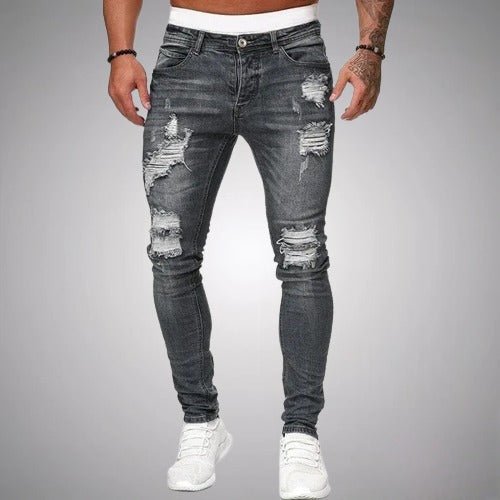 Frontansicht der enganliegenden, zerrissenen Jeans in verwaschenem Anthrazitgrau mit weißen Sneakern vor grauem Hintergrund.
