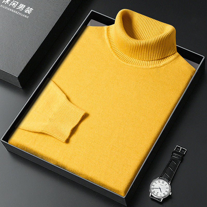Gelber Rollkragenpullover gefaltet in einer schwarzen Box, daneben eine Armbanduhr mit hellem Zifferblatt und Lederarmband; die Geschenkverpackung steht links d