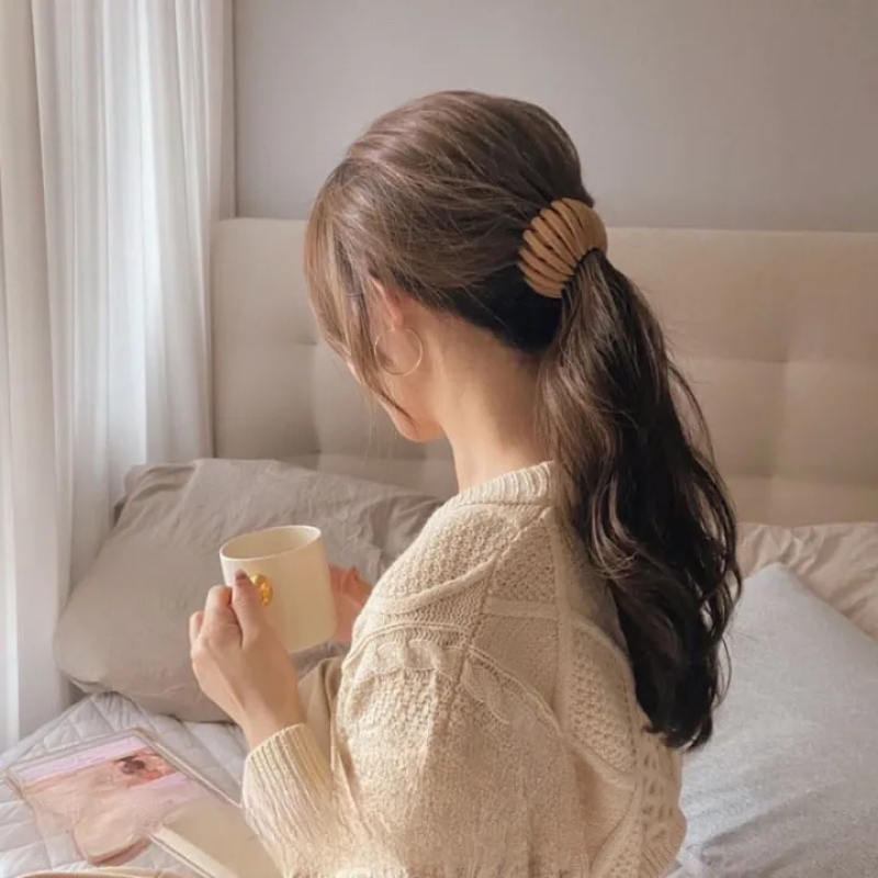 Haarklammer in Beige im Haar von hinten, daneben eine Tasse und ein Strickpullover.