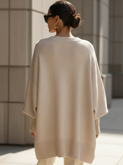 Rückansicht des beigen Strickponchos mit breitem Rippsaum, getragen mit weißer Hose und Sonnenbrille 5