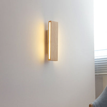 Senkrecht montierte Holz-Wandleuchte mit leuchtendem Seitenstreifen an einer Wand neben Fenster mit Jalousie und Stuhl.