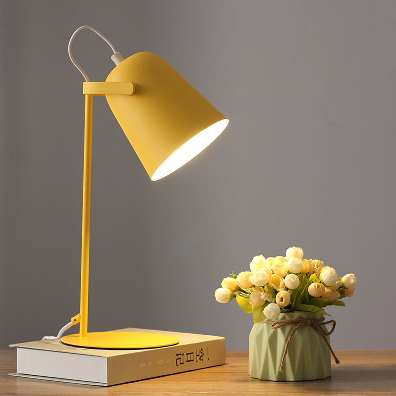 Gelbe Tischlampe mit eimerförmigem Schirm steht eingeschaltet auf einem Buch, daneben ein Väschen mit hellen Röschen. 1