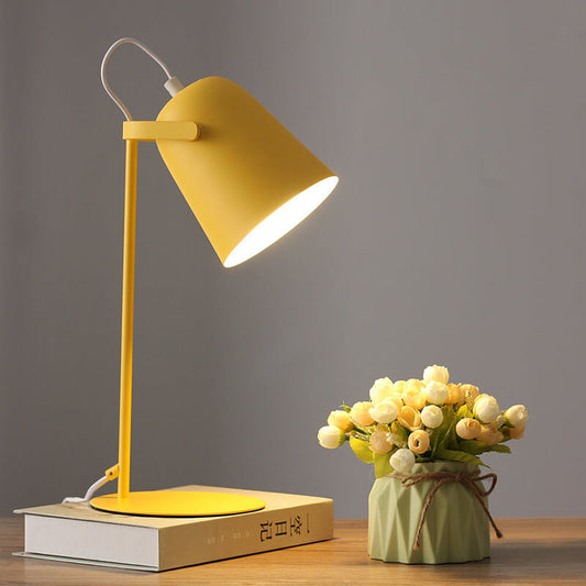 Gelbe Tischlampe mit eimerförmigem Schirm steht eingeschaltet auf einem Buch, daneben ein Väschen mit hellen Röschen. 1
