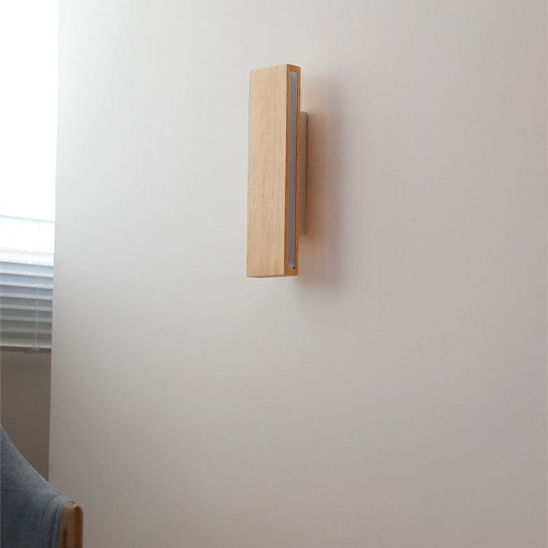Ausgeschaltete Wandleuchte aus hellem Holz mit weißer Halterung, seitlich neben einem Fenster mit Jalousie.