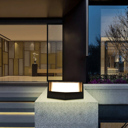 Fünfeckige schwarze Leuchte auf einem Steinsockel vor einem modernen Hauseingang mit Glasfront, abends beleuchtet.