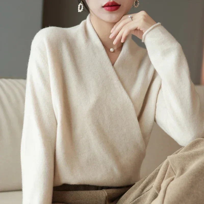 Cremeweißer Wickelpullover, Frau stützt das Kinn auf die Hand, dazu eine beige Hose 10