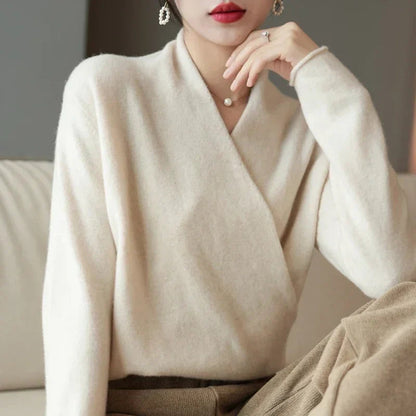 Cremeweißer Wickelpullover, Frau stützt das Kinn auf die Hand, dazu eine beige Hose 10