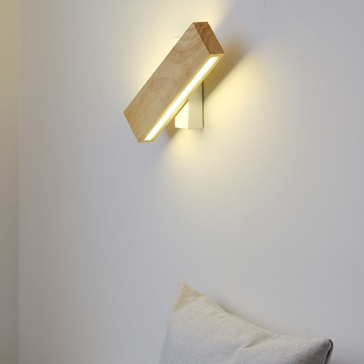 Eingeschaltete LED-Wandleuchte mit Holzbalken und weißer Halterung, schräg gedreht, an heller Wand.