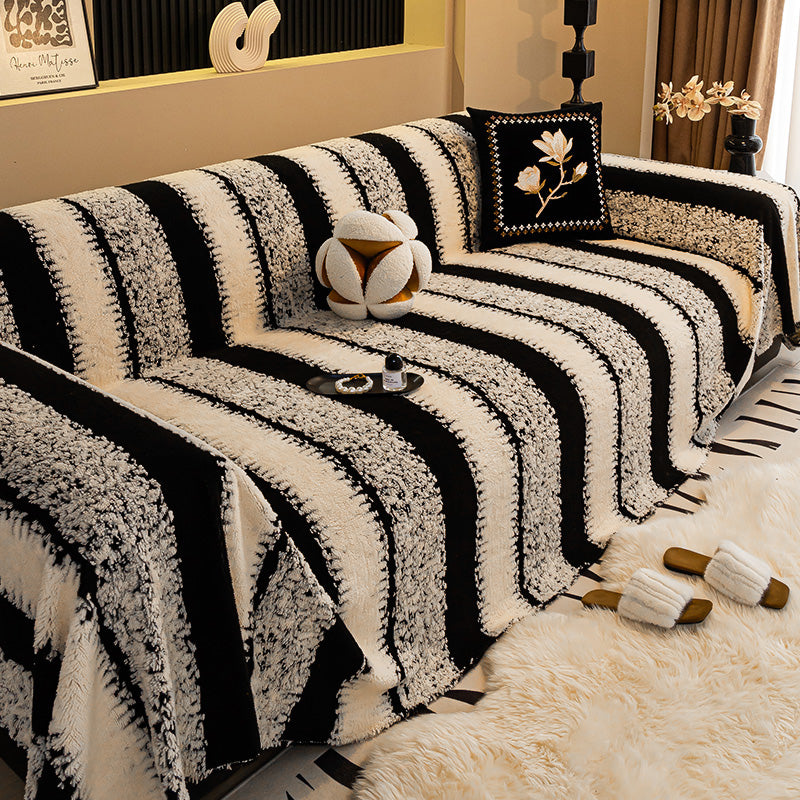 Sofa mit breit gestreiftem Plüschüberwurf in Schwarz und Creme, davor Fellteppich und Pantoffeln 9