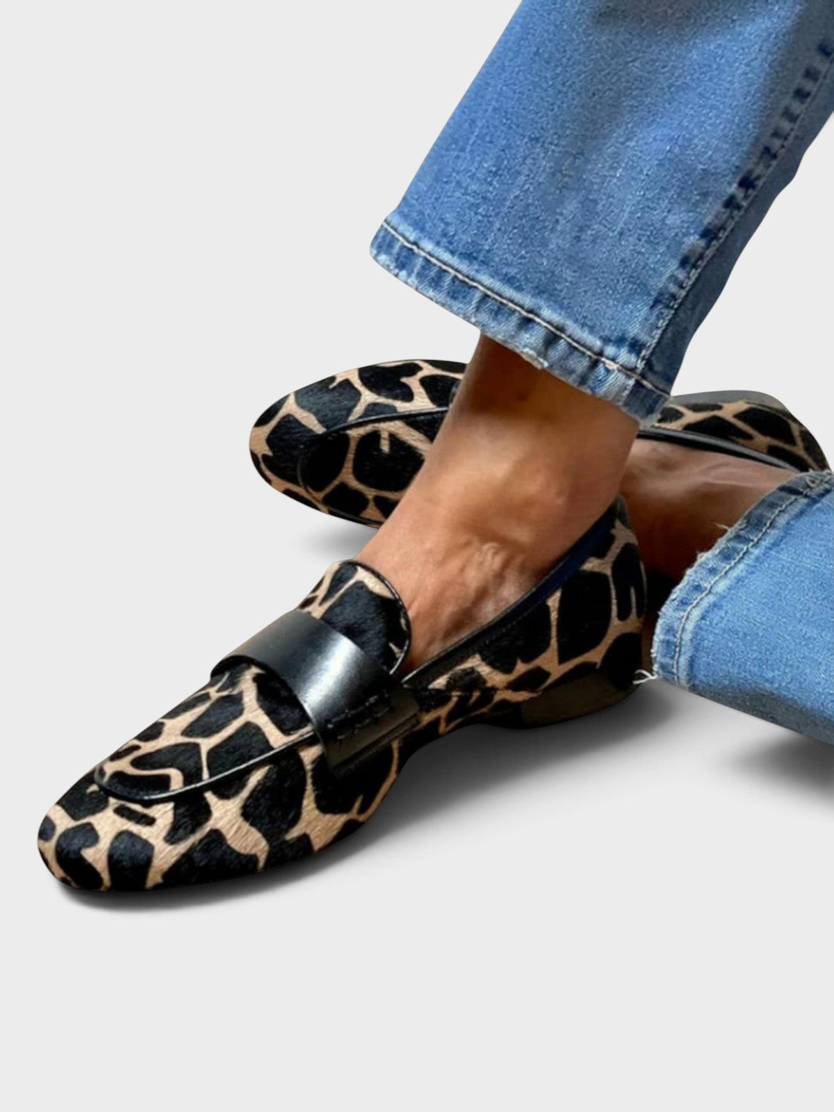 Getragener Loafer mit beige-schwarzem Fellmuster und schwarzem Lederband, Seitenansicht auf hellem Hintergrund.