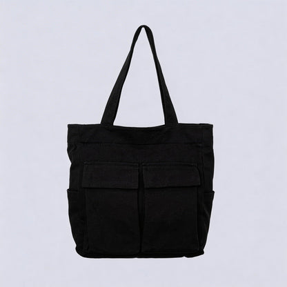 Schwarze Tote Bag aus Stoff mit zwei aufgesetzten Klappentaschen vorn und seitlichen Einstecktaschen, freigestellt vor hellem Hintergrund.