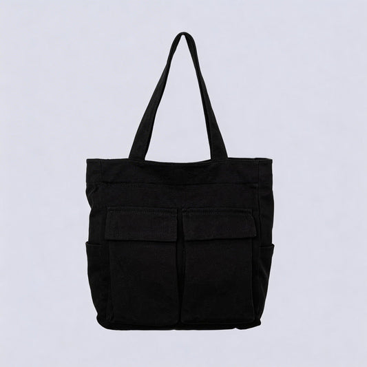 Schwarze Tote Bag aus Stoff mit zwei aufgesetzten Klappentaschen vorn und seitlichen Einstecktaschen, freigestellt vor hellem Hintergrund.