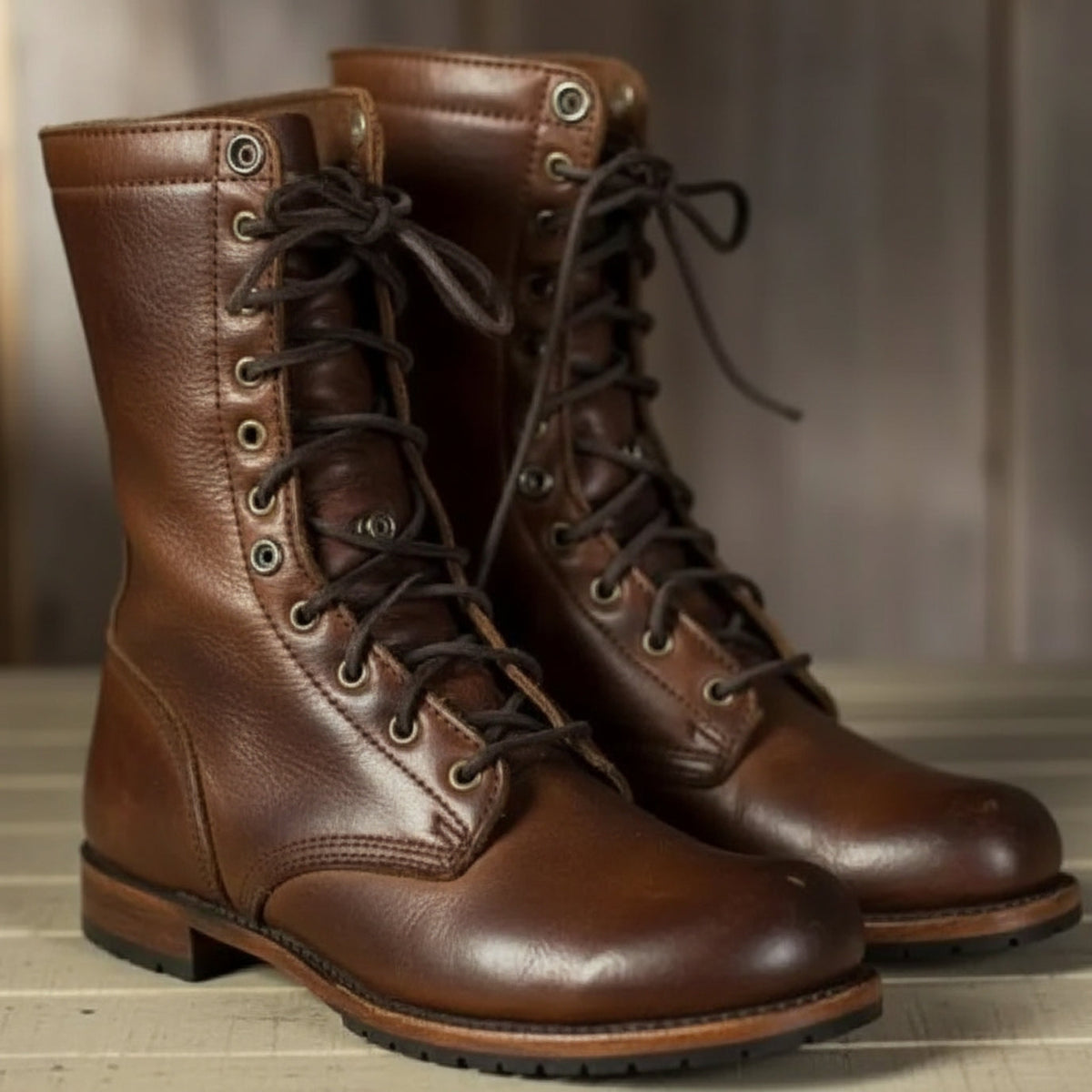 Braune Leder-Schnürstiefel mit dunklen Schnürsenkeln und Metallösen, schräg von vorn auf einem hellen Holzboden.