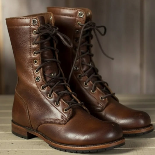 Braune Leder-Schnürstiefel mit dunklen Schnürsenkeln und Metallösen, schräg von vorn auf einem hellen Holzboden.
