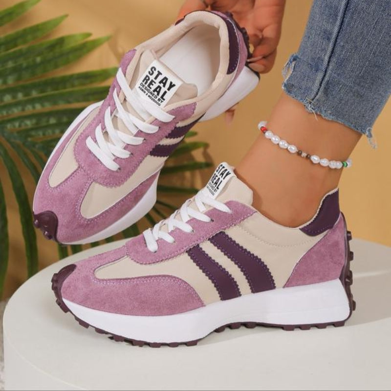 Rosa-beige Sneaker mit violetten Streifen, getragen vor Palmenblatt, ein Schuh angehoben, Schnürung und Zunge sichtbar 11