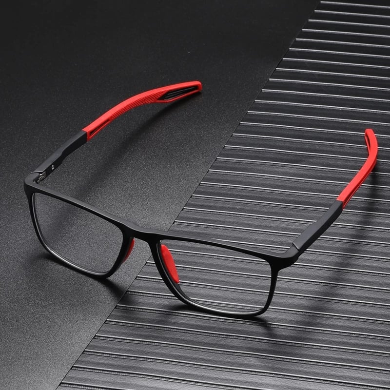 Schwarze Brille mit roten Bügelenden und roten Nasenpads, aufgeklappt auf dunkler, gerillter Oberfläche liegend. 8