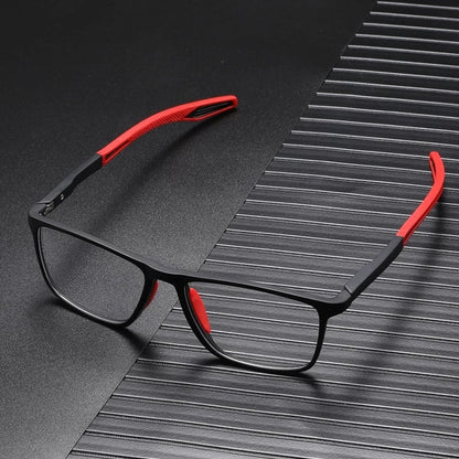Schwarze Brille mit roten Bügelenden und roten Nasenpads, aufgeklappt auf dunkler, gerillter Oberfläche liegend. 8