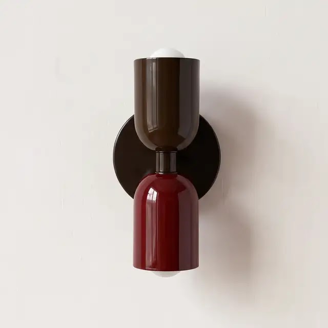 Wandlampe mit dunkelbraunem oberem und weinrotem unterem Schirm an einer schwarzen runden Wandplatte, frontal vor heller Wand. 24