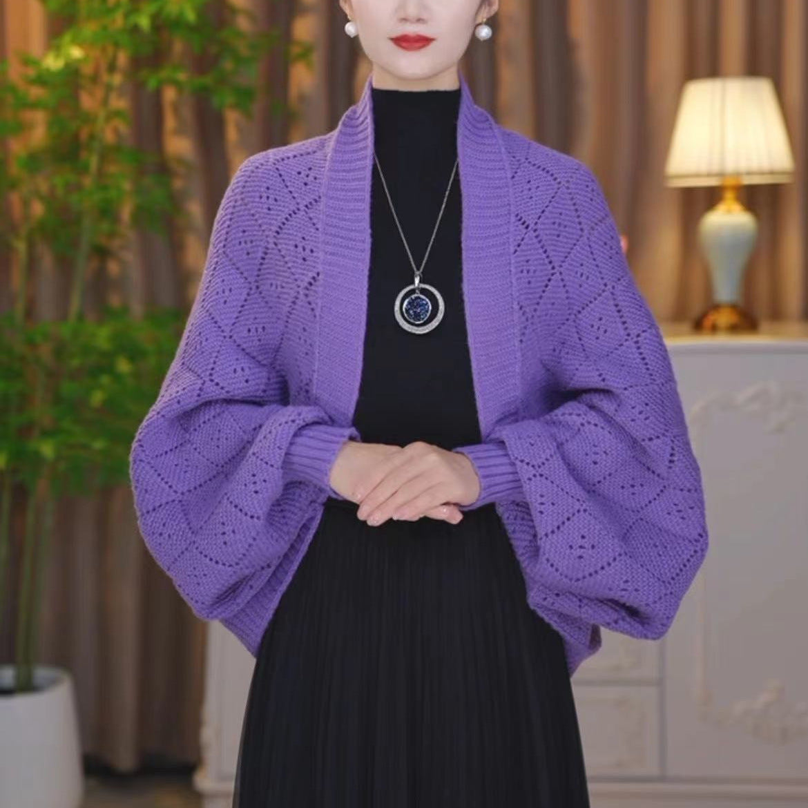 Violette Strickjacke mit durchbrochenem Rautenmuster und weiten Ärmeln, getragen vor Vorhang und Pflanze 15