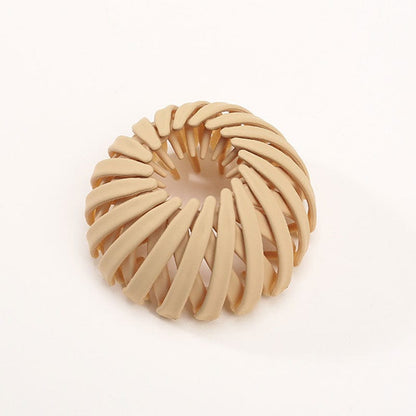 Matte Haarklammer in Sandbeige mit spiralförmig angeordneten Rippen, einzeln vor hellem Hintergrund.