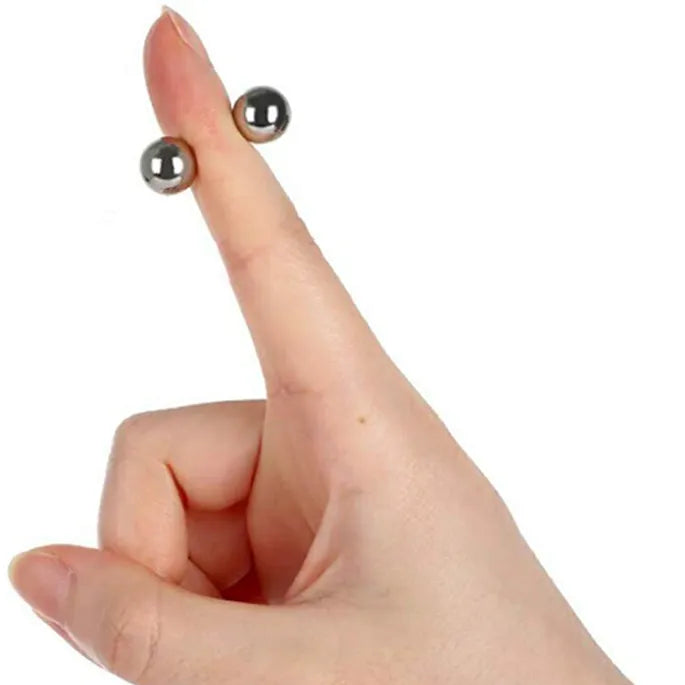 Zeigefinger mit zwei kleinen silbernen Magnetkugeln, die sich magnetisch halten.