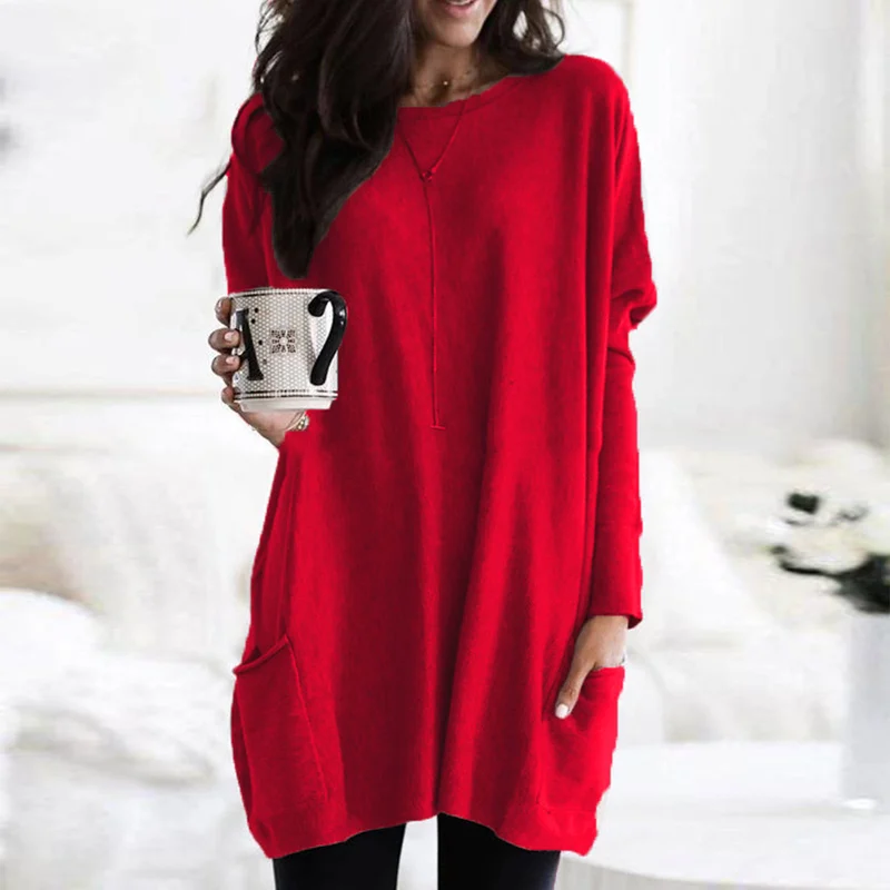 Frau in rotem Oversize-Pullover hält Tasse, gemütliche Wintermode, Wohnzimmer-Hintergrund.