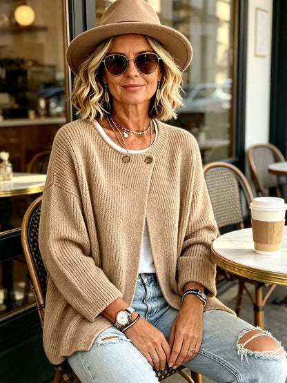 Frau mit Hut und Sonnenbrille trägt die camelfarbene Strickjacke sitzend vor einem Café 5
