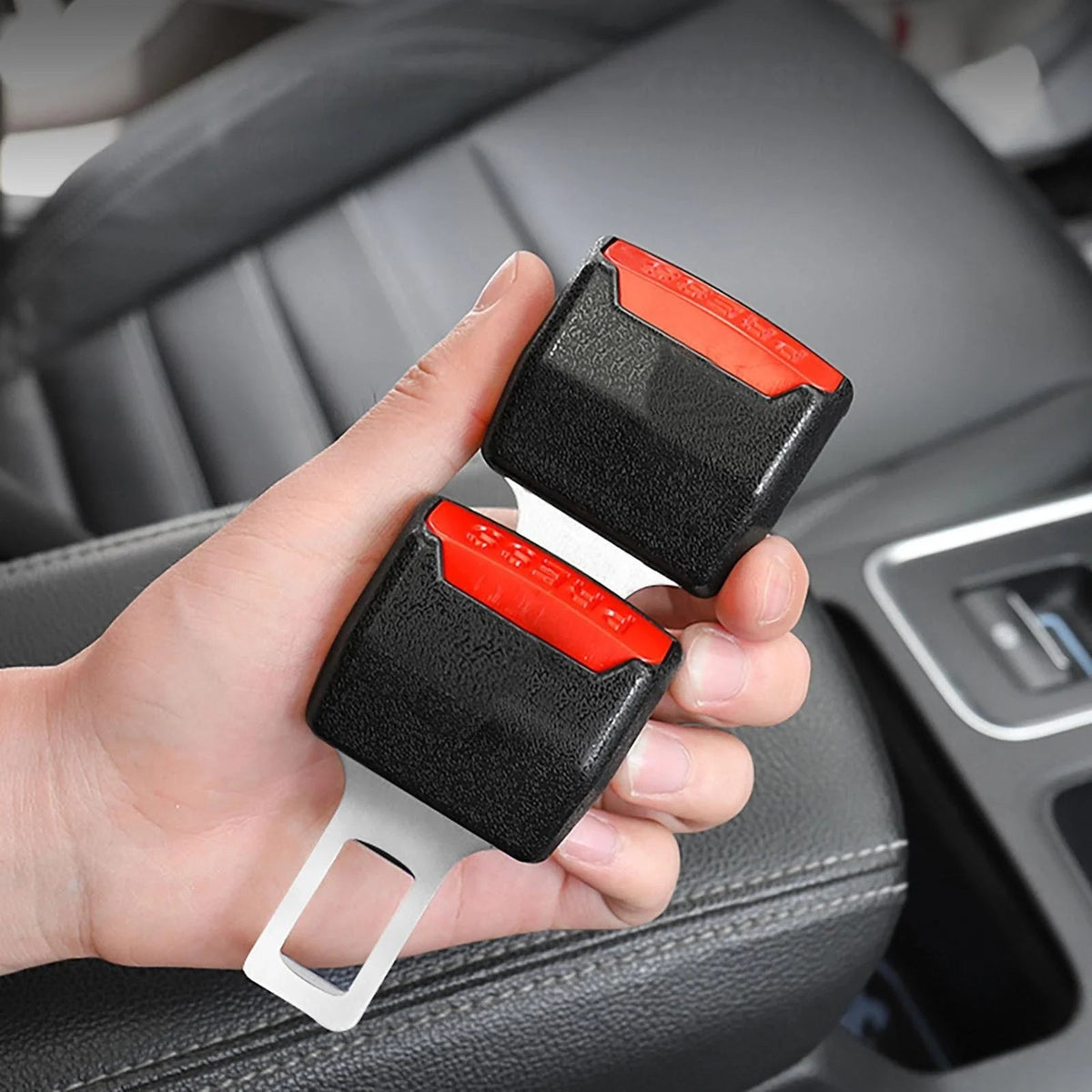 Hand hält zwei schwarze Gurtschloss-Einsätze mit rotem Knopf und Metallzunge im Auto, davor Sitz und Mittelkonsole 2
