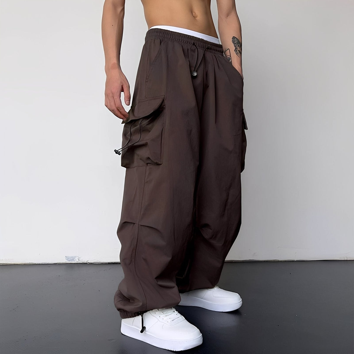 Weite Cargohose in Dunkelbraun, am Model mit weißen Sneakern, Seitentaschen, Kordelzug und elastischem Saum 6