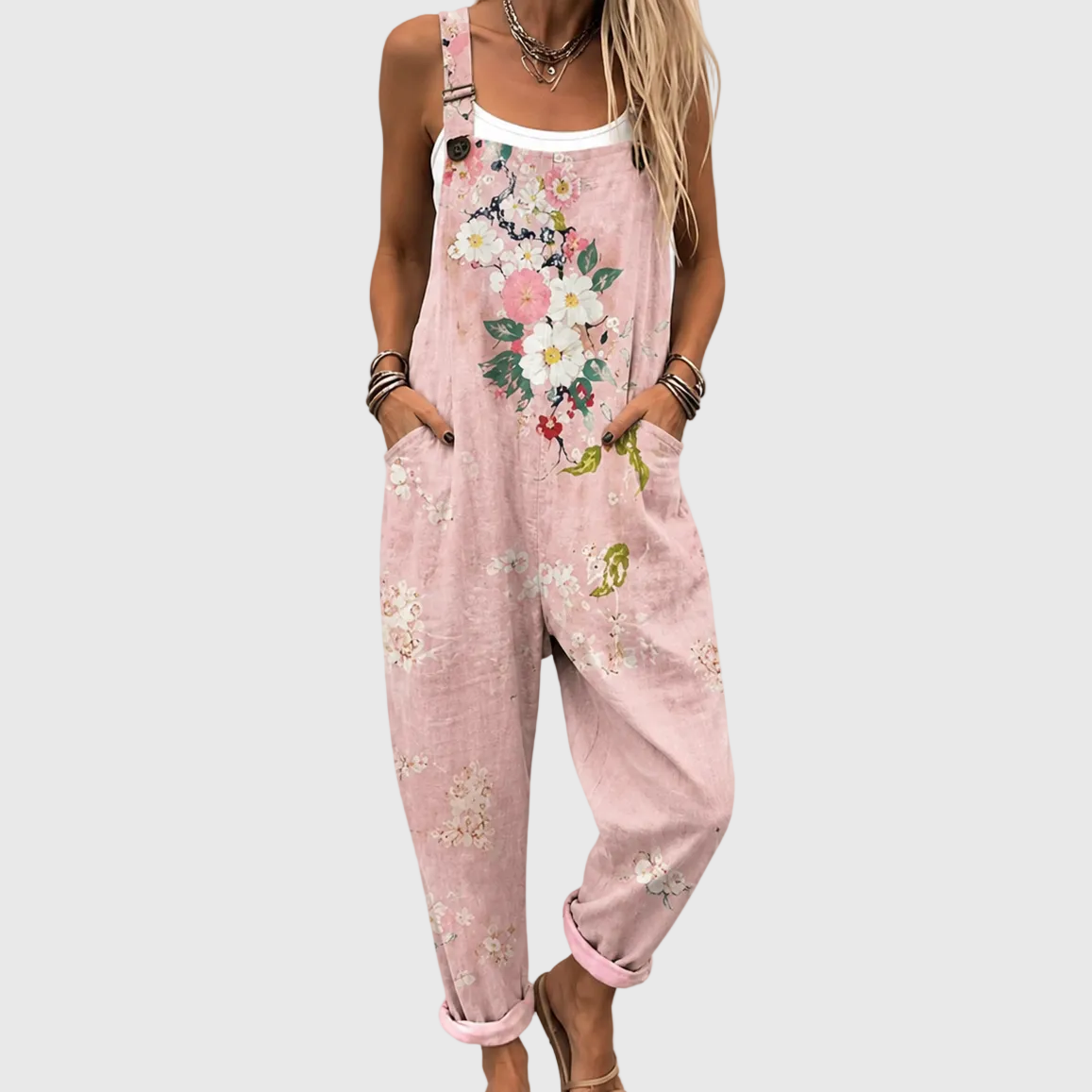 Nahaufnahme der Latzhose am Model, Hände in den Seitentaschen, großes Blumenmotiv auf der Brust, darunter ein weißes Top. 1
