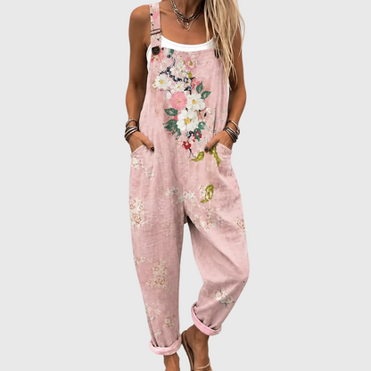 Nahaufnahme der Latzhose am Model, Hände in den Seitentaschen, großes Blumenmotiv auf der Brust, darunter ein weißes Top. 1