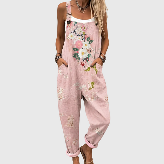 Nahaufnahme der Latzhose am Model, Hände in den Seitentaschen, großes Blumenmotiv auf der Brust, darunter ein weißes Top. 1