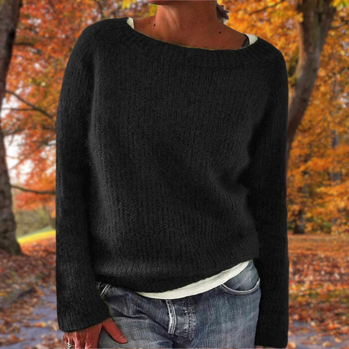 Schwarzer Strickpullover mit rundem Ausschnitt, von einer Frau über weißem Shirt und Jeans im Herbstwald getragen. 2