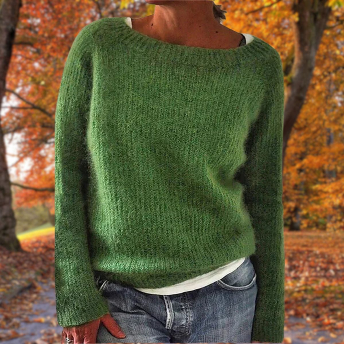 Grüner Strickpullover mit langen Ärmeln, getragen mit weißem Shirt und Jeans vor einer Kulisse aus Herbstlaub. 5