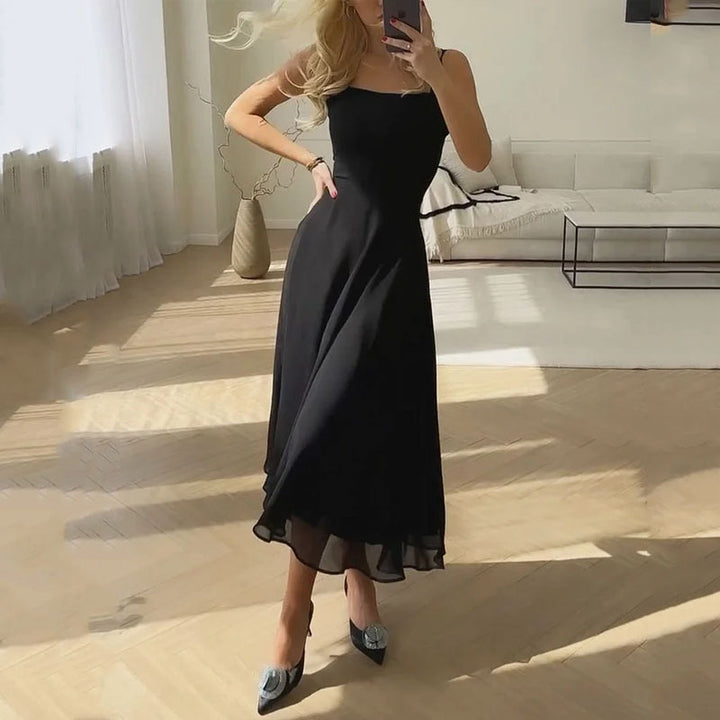 Frau in elegantem schwarzem Abendkleid posiert im sonnigen Wohnzimmer.