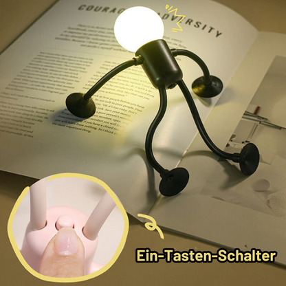 Schwarzes Nachtlicht steht auf einem aufgeschlagenen Buch und beleuchtet die Seiten; Ausschnitt zeigt den Ein-Tasten-Schalter am rosa Modell. 10