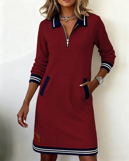 Weinrotes Langarmkleid in Frontansicht mit gestreiften Bündchen und Saum, mit einer Hand in der Tasche.