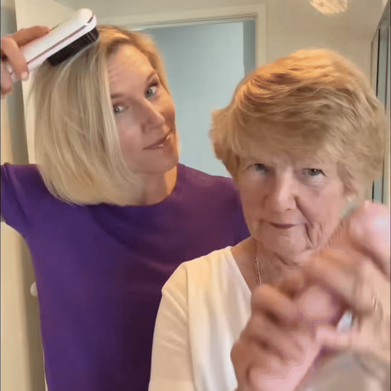 Blonde Frau stylt mit einer weißen Bürste ihr Haar und steht hinter einer älteren Frau mit kurzem Haar. 9