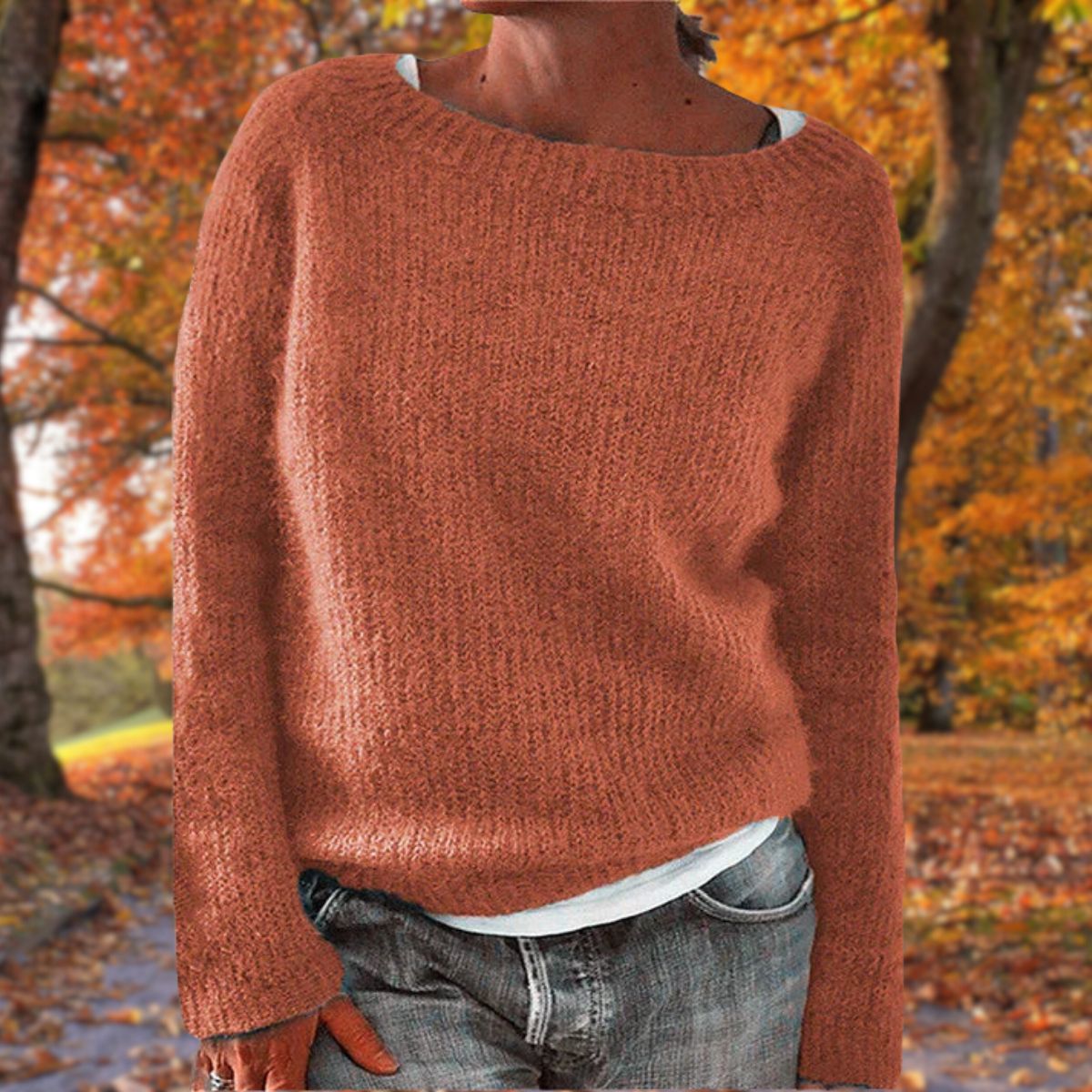 Rostroter Strickpullover mit rundem Ausschnitt, getragen über weißem Shirt und grauer Jeans zwischen Herbstbäumen. 6